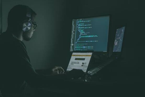 A person coding in a dark environment, focusing on their laptop screen in a dimly lit room.