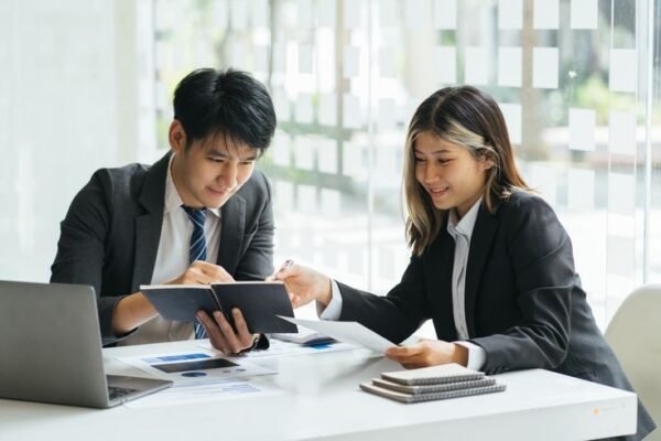 Two business professionals reviewing executive hiring documents and reports during an executive search meeting in an office setting in Indonesia